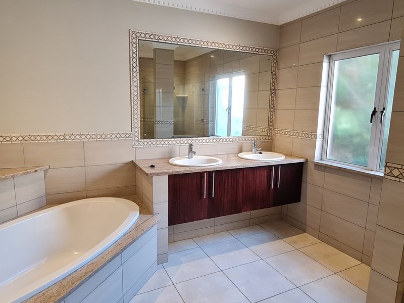 Spacious bathroom featuring a double vanity, built-in bathtub, glass shower enclosure, and neutral wall and floor tiling.
