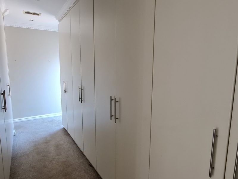 A spacious walk-in dressing area featuring extensive floor-to-ceiling built-in cabinetry, neutral carpeting, and elegant crown molding.