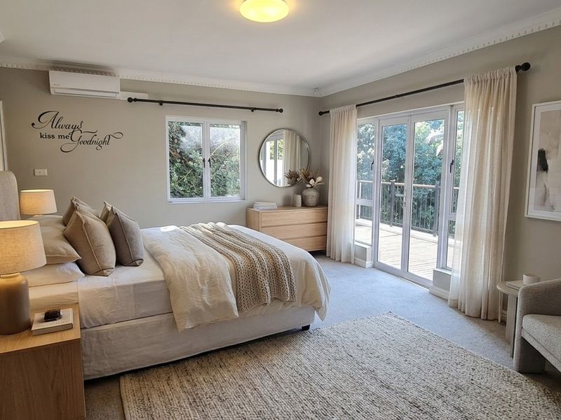 Spacious bedroom featuring neutral tones, split-system air conditioning, and direct access to a private balcony through glass french doors.