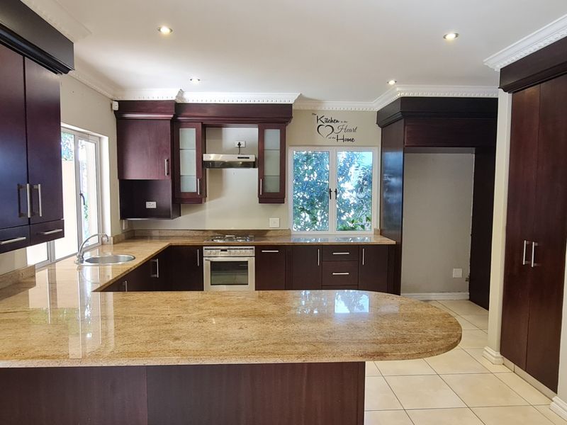 A spacious kitchen featuring dark wood cabinetry, granite countertops, built-in oven with gas hob, and tiled flooring in a well-maintained condition.