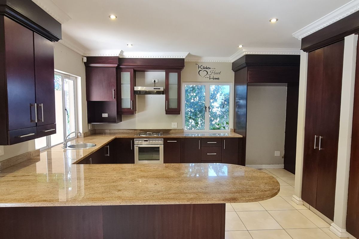A spacious kitchen featuring dark wood cabinetry, granite countertops, built-in oven with gas hob, and tiled flooring in a well-maintained condition.