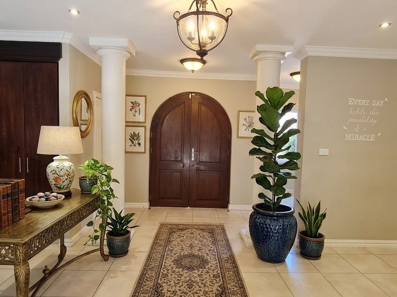 Spacious and welcoming entrance hall featuring elegant arched double doors, decorative columns, crown molding, and neutral tiled flooring.