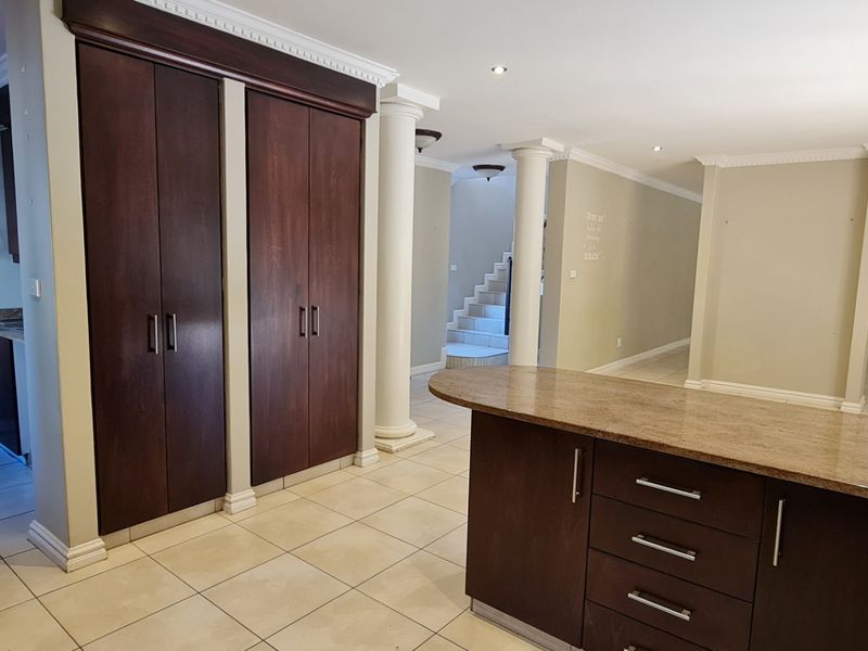 Spacious open-plan living area featuring dark wood cabinetry, granite countertops, decorative cornices, and tiled flooring, leading to a staircase and additional living space.