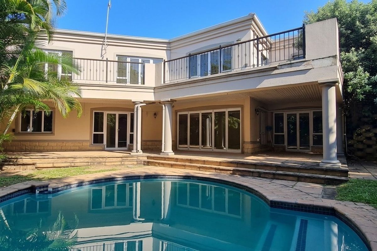 Rear view of the townhouse featuring a swimming pool, paved patio area, and an upper-level balcony with wrought iron railings.