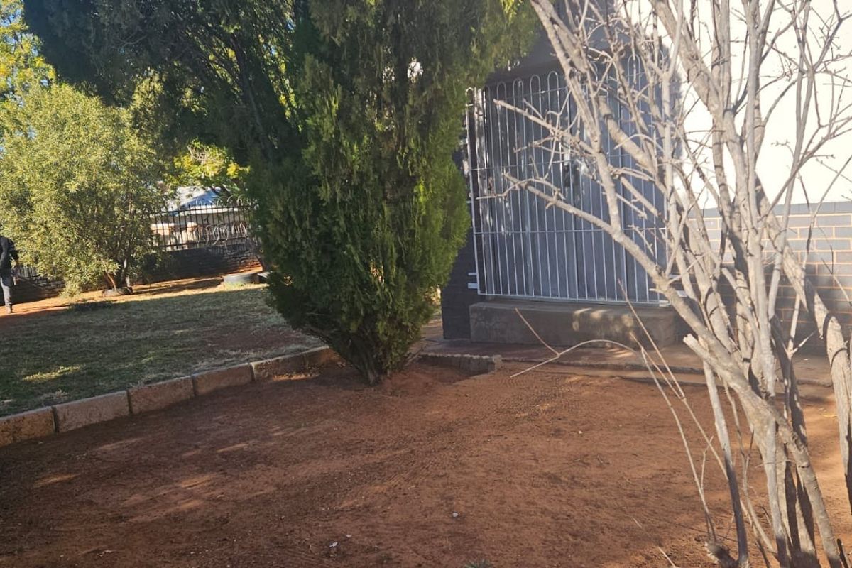 A view of the rear garden area featuring a security gate, brick exterior wall, and perimeter fencing.