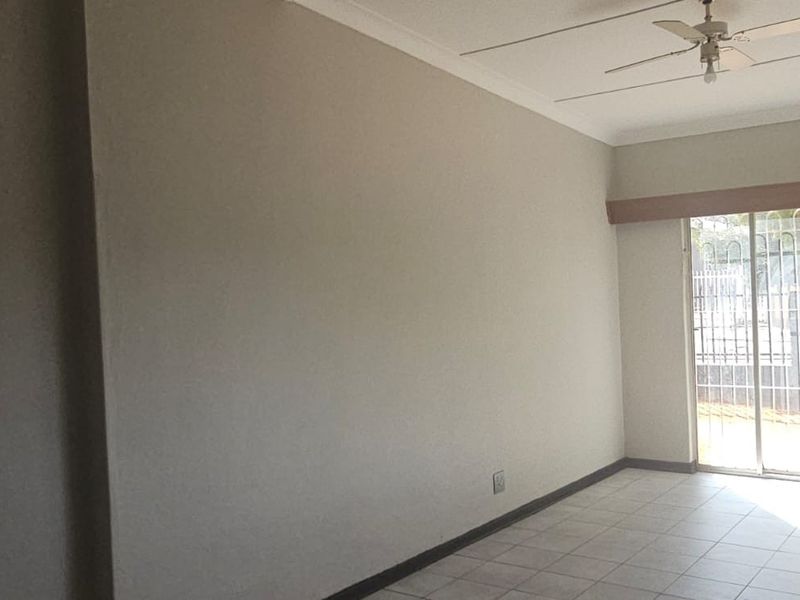 A spacious, empty living area featuring neutral walls, tiled flooring, a ceiling fan, and large sliding glass doors leading to the exterior.