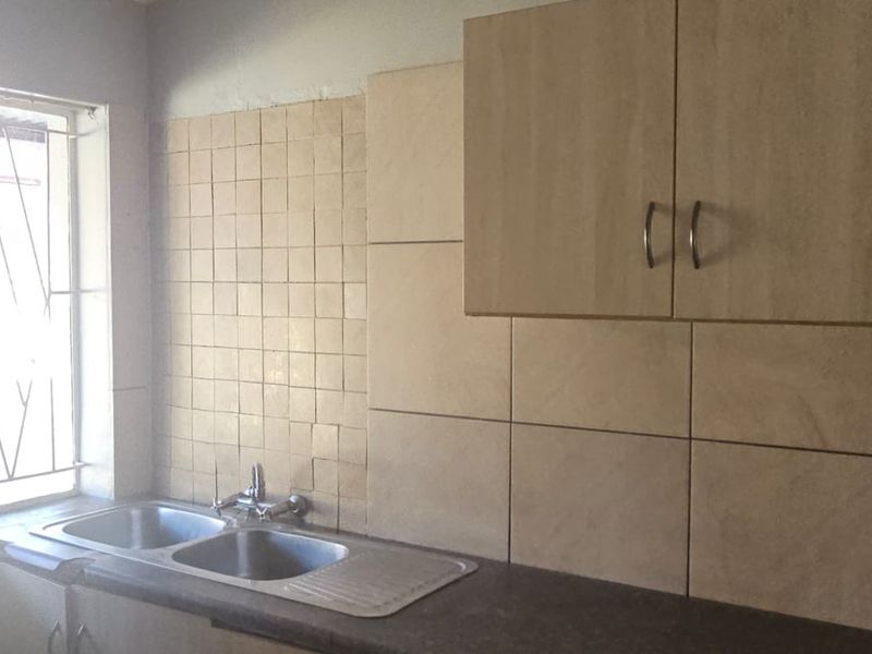 A functional kitchen area featuring a double bowl stainless steel sink, laminate cabinetry, and tiled splashbacks, requiring cosmetic updates to modernize the space.