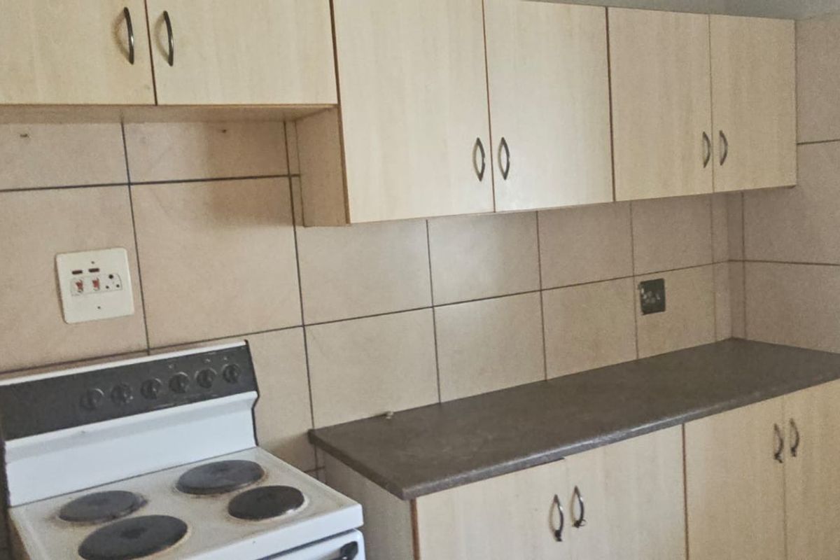 A functional kitchen featuring light wood-look cabinetry, dark countertops, and full-height ceramic wall tiling with a freestanding electric stove.