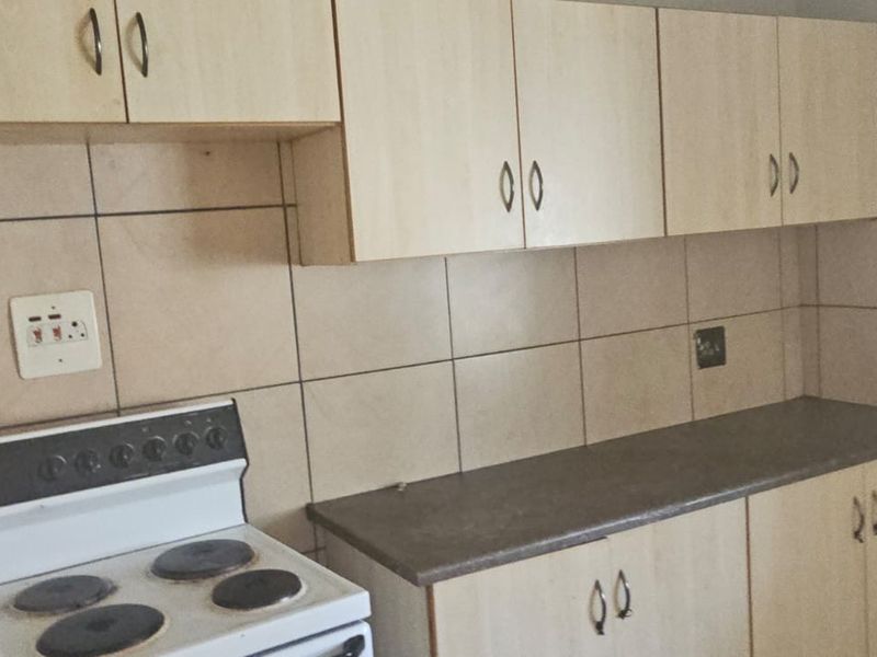 A functional kitchen featuring light wood-look cabinetry, dark countertops, and full-height ceramic wall tiling with a freestanding electric stove.