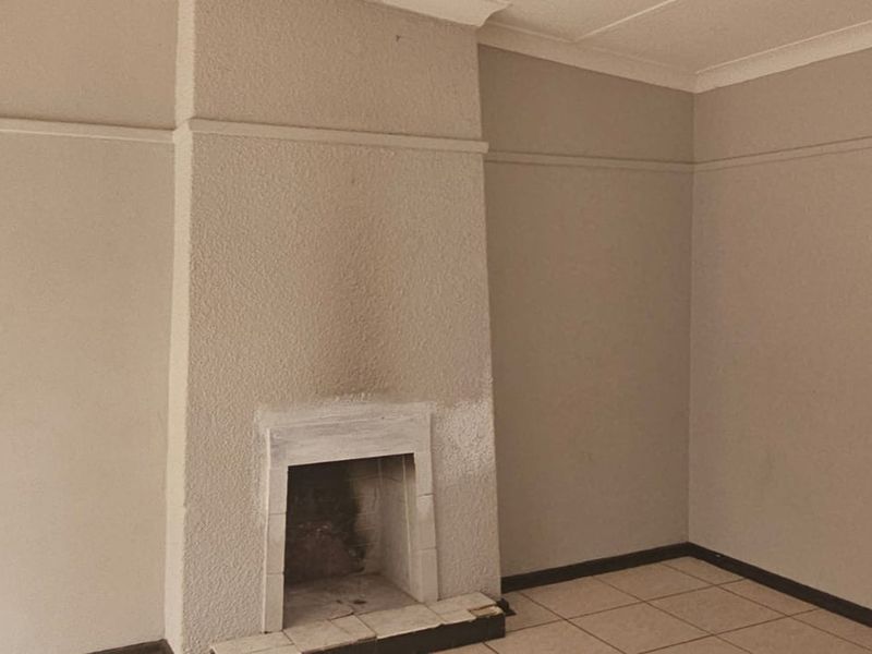 An empty living room featuring a central fireplace with a textured finish, tiled flooring, and coved ceilings, offering a blank canvas for interior design.