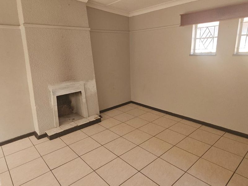 An empty living room featuring tiled flooring, a built-in fireplace with soot staining, and leaded glass windows.