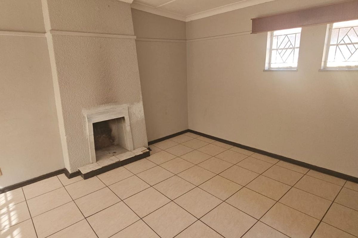 An empty living room featuring tiled flooring, a built-in fireplace with soot staining, and leaded glass windows.