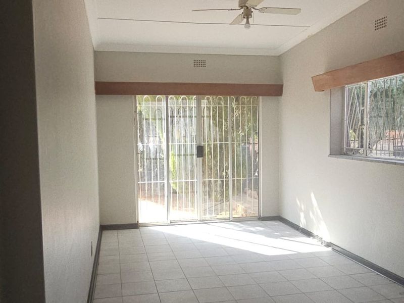 A bright, empty living area featuring tiled floors, a ceiling fan, and a sliding glass door with security gate leading to the exterior.