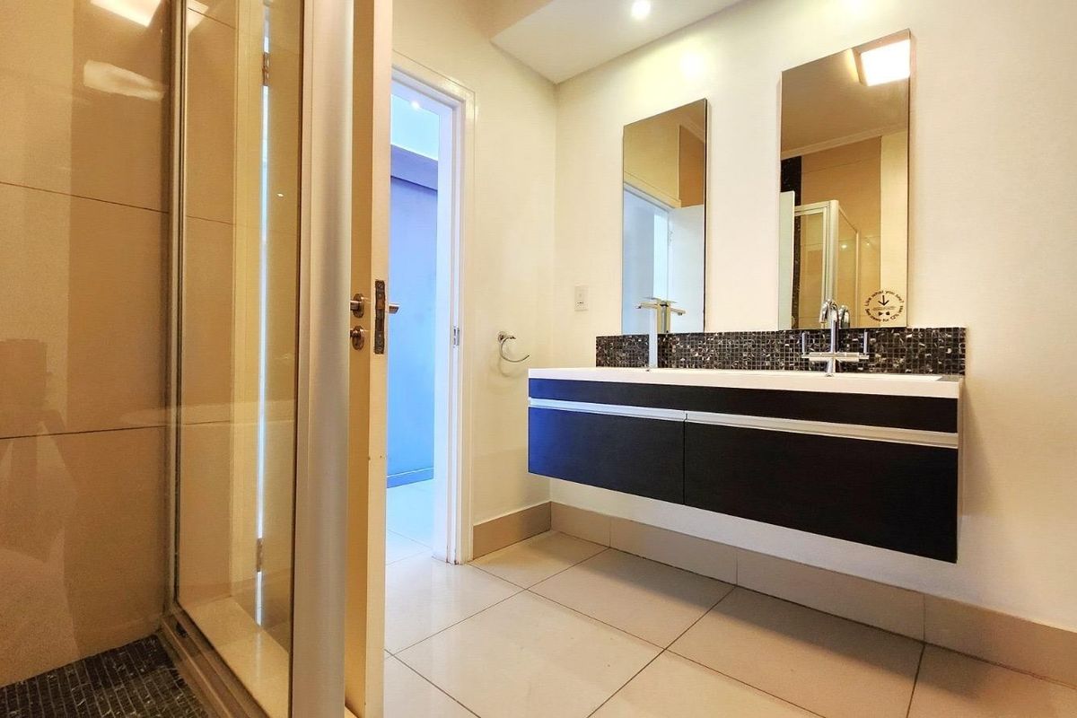 Modern bathroom featuring a sleek wall-mounted double vanity with mosaic backsplash, large mirrors, and a spacious glass-enclosed shower.