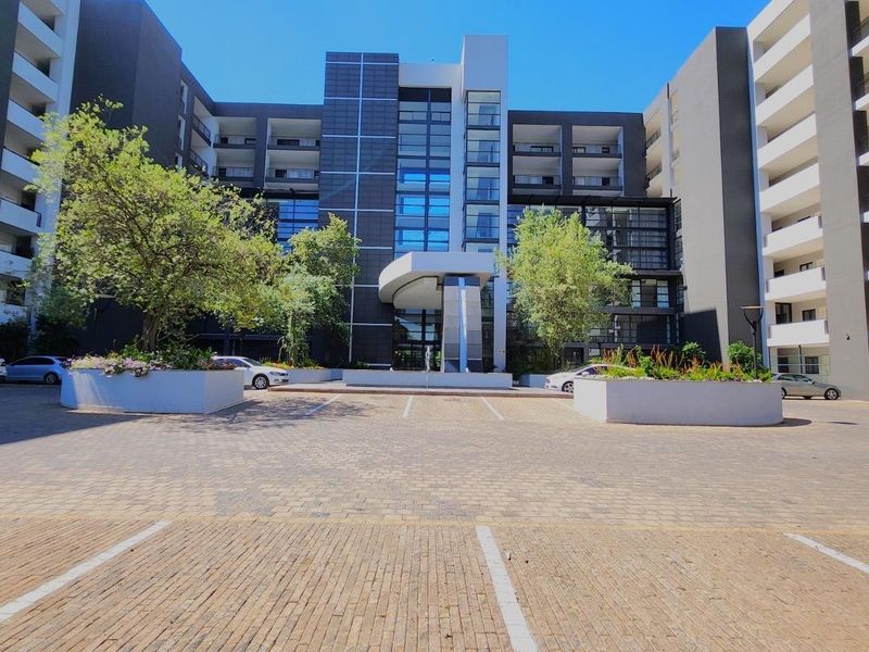 Modern multi-story apartment complex featuring a paved entrance courtyard, glass facade elements, and a covered architectural canopy.
