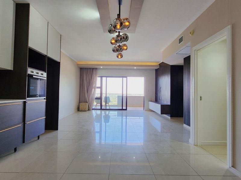 Modern open-plan living area featuring a sleek kitchen with built-in oven, tiled floors, and sliding doors leading to a balcony.
