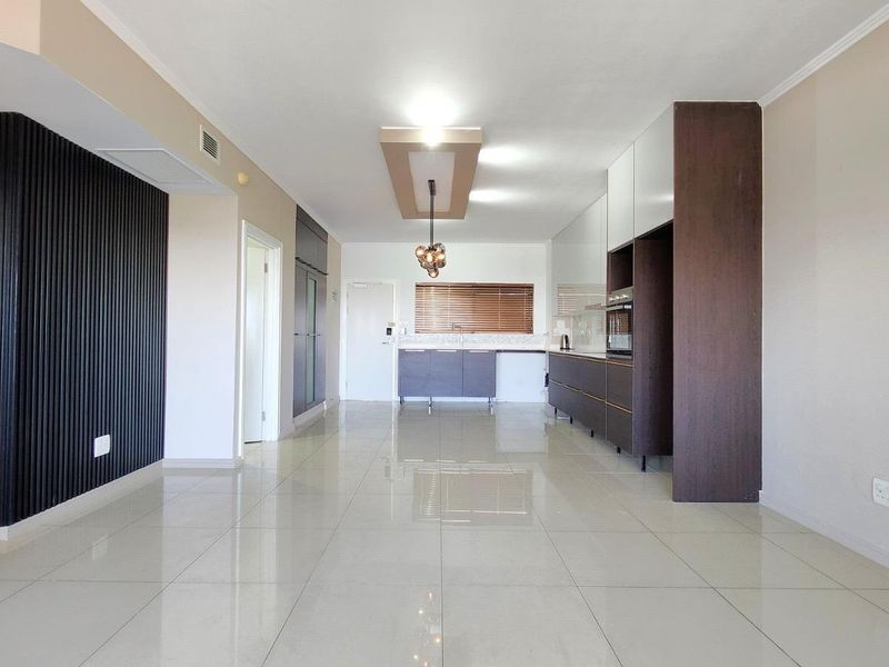Spacious open-plan living and kitchen area featuring modern built-in cabinetry, sleek tiled flooring, and a contemporary slatted feature wall.