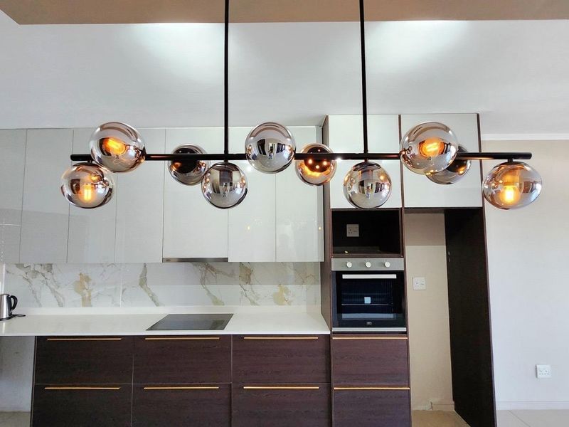 Modern kitchen featuring sleek glossy cabinetry, built-in oven, electric hob, and a stylish contemporary pendant light fixture.