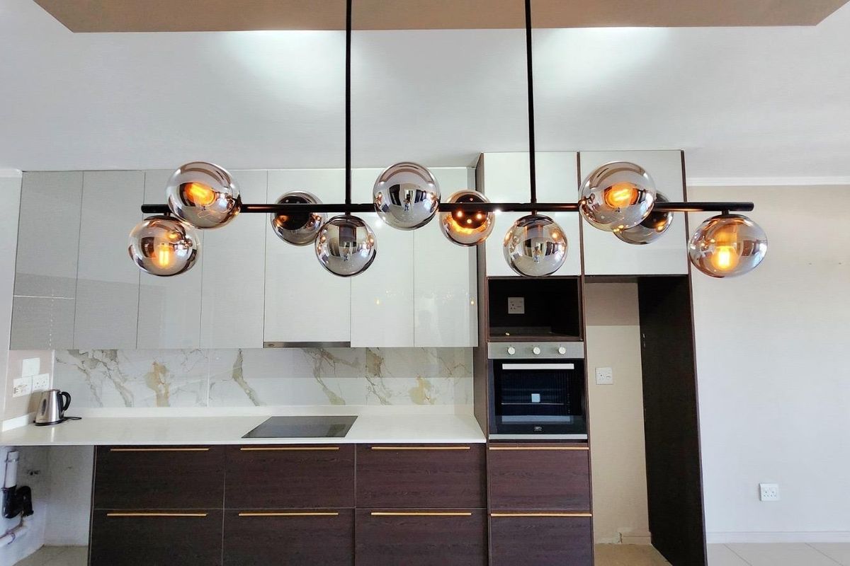 Modern kitchen featuring sleek glossy cabinetry, built-in oven, electric hob, and a stylish contemporary pendant light fixture.