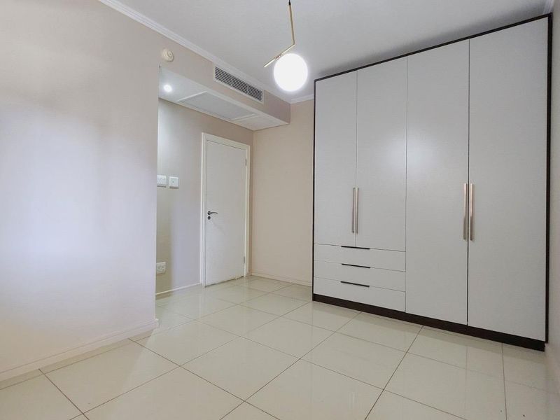 A clean, modern bedroom featuring large built-in wardrobes, neutral tiled flooring, and integrated ducted air conditioning.