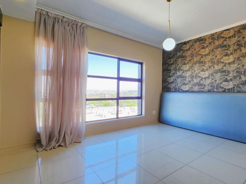 A bright, spacious bedroom featuring large windows with natural light, tiled flooring, and a feature wall with decorative wallpaper.