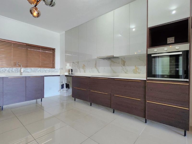 Modern kitchen featuring high-gloss cabinetry, built-in oven, stone countertops, and sleek tiled splashbacks with polished porcelain flooring.