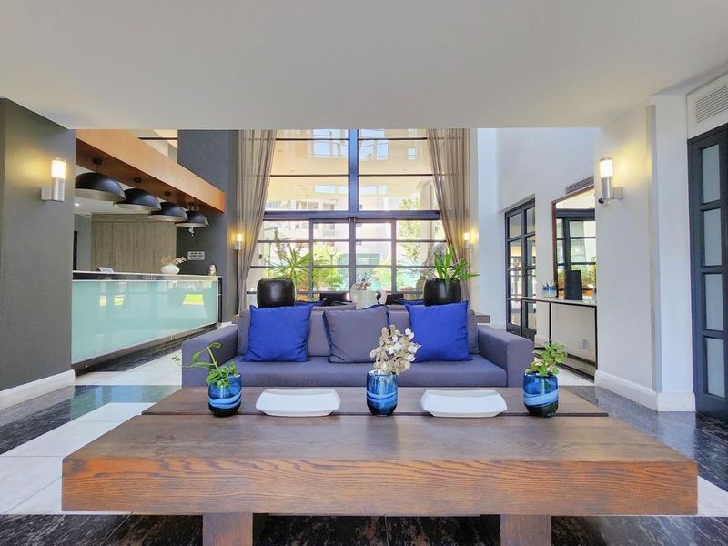 Spacious living area featuring double volume ceilings, large glass windows for natural light, and modern tiled flooring in a well-maintained apartment setting.