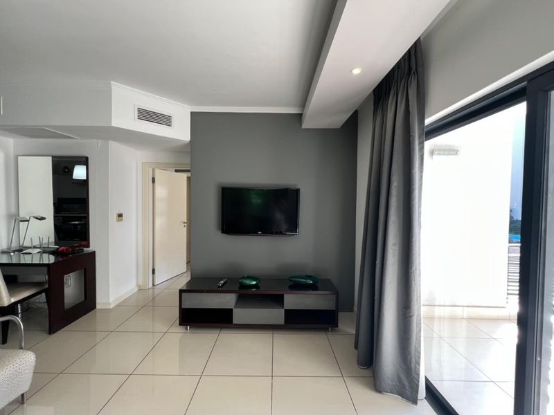 Modern living room featuring neutral tiled flooring, a feature wall with wall-mounted television, and large sliding glass doors leading to an outdoor balcony.