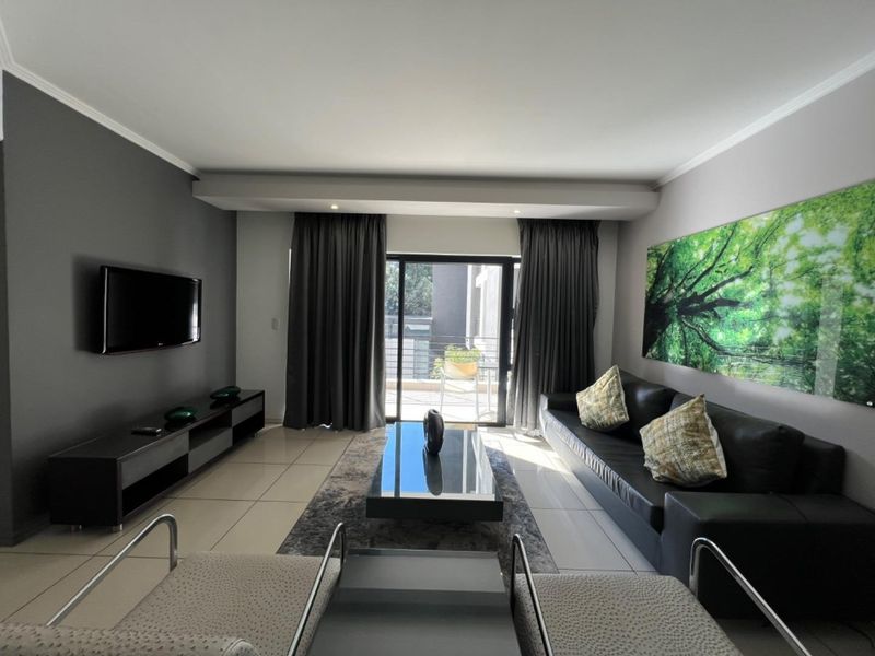 A modern living room featuring tiled floors, neutral grey walls, and a sliding glass door providing access to an outdoor balcony area.