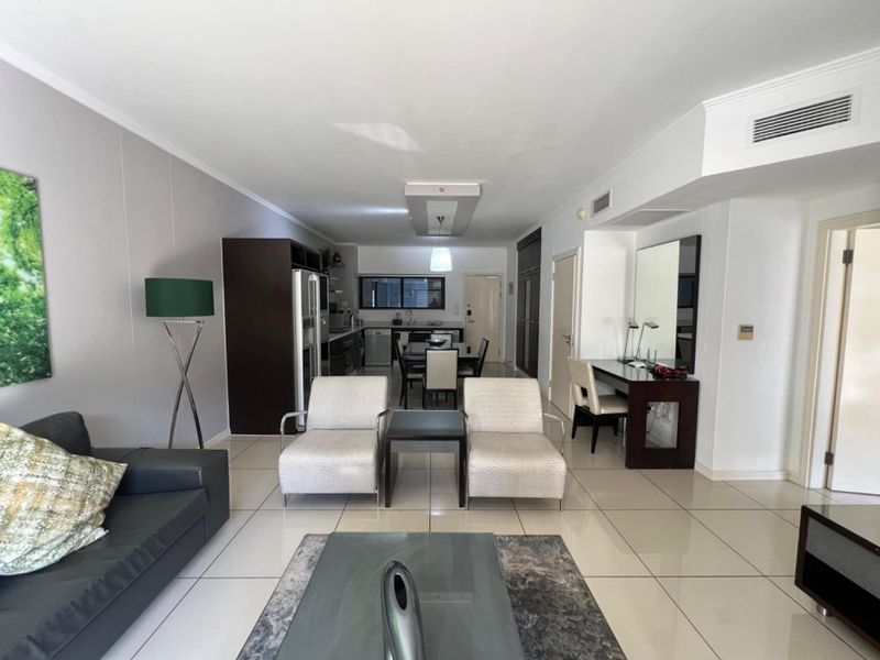 Spacious open-plan living and kitchen area featuring neutral tiled flooring, modern recessed lighting, and integrated cabinetry, offering a functional and versatile living space.