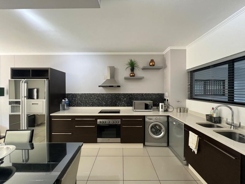 Modern kitchen featuring dark cabinetry, stone countertops, integrated appliances, and a sleek tiled splashback, offering a functional and contemporary cooking space.