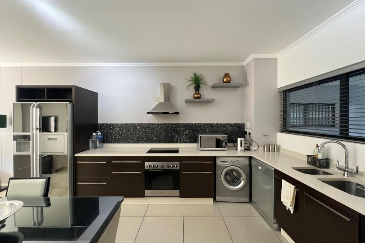 Modern kitchen featuring dark cabinetry, stone countertops, integrated appliances, and a sleek tiled splashback, offering a functional and contemporary cooking space.