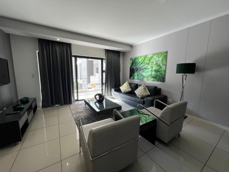 A modern, well-maintained living room featuring large format floor tiles, recessed lighting, and a sliding glass door providing access to an outdoor balcony.