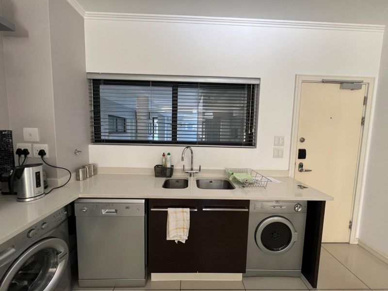 A functional kitchen area featuring dark wood cabinetry, stone countertops, a double stainless steel sink, and integrated laundry and dishwasher appliances.