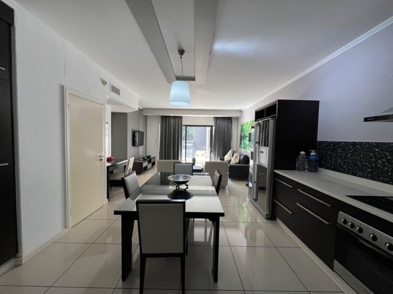 Modern open-plan living area featuring a sleek kitchen with stone countertops, integrated appliances, and tiled flooring, flowing seamlessly into the dining and lounge space.