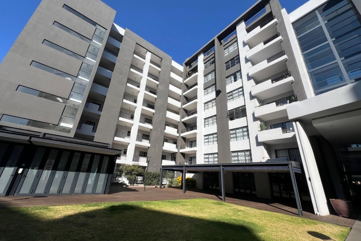 A view of the apartment complex rear facade featuring multi-story balconies, a wooden deck, and a well-maintained lawn area.