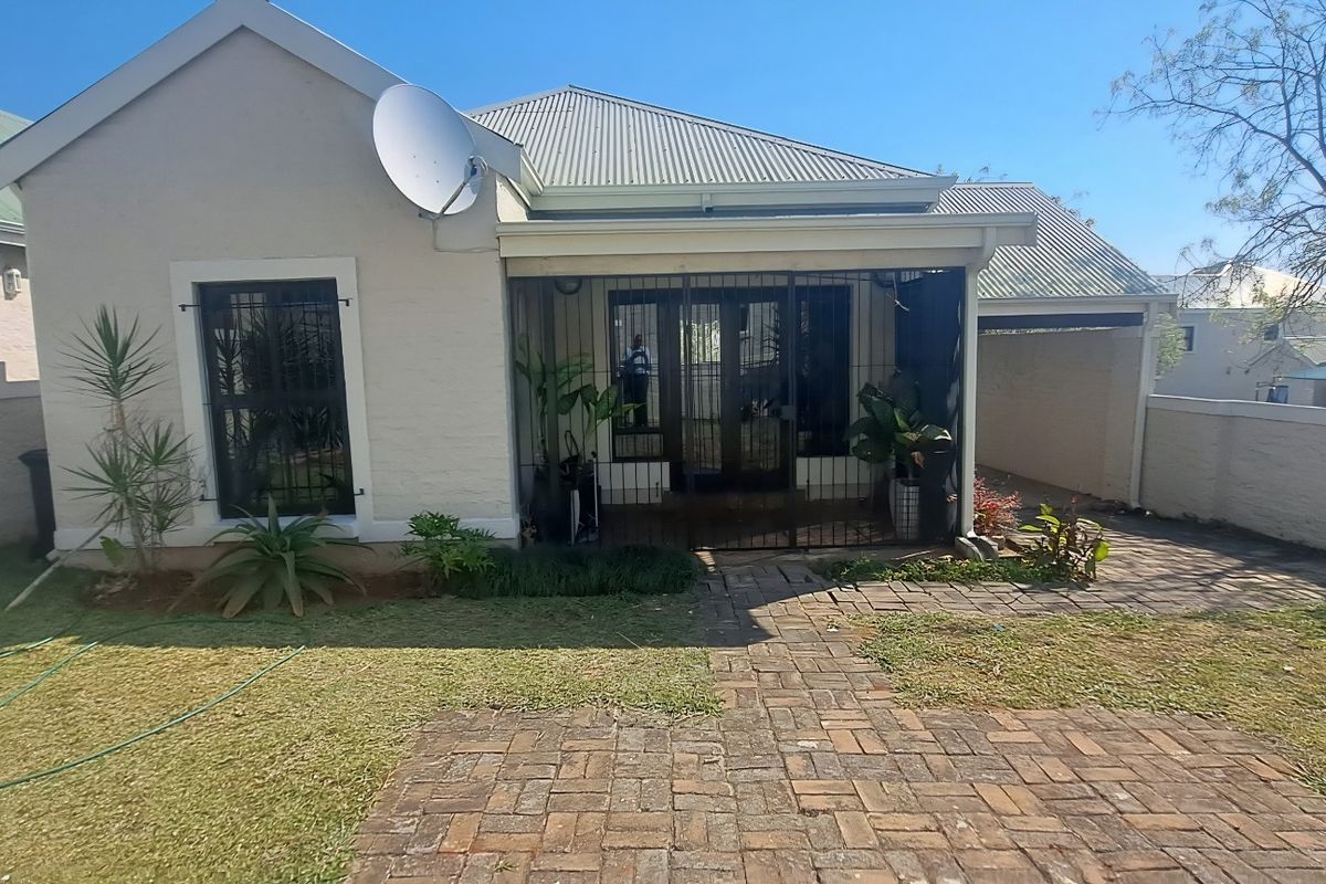 Rear view of the townhouse featuring a paved walkway, covered patio area, and enclosed garden space with boundary walls.