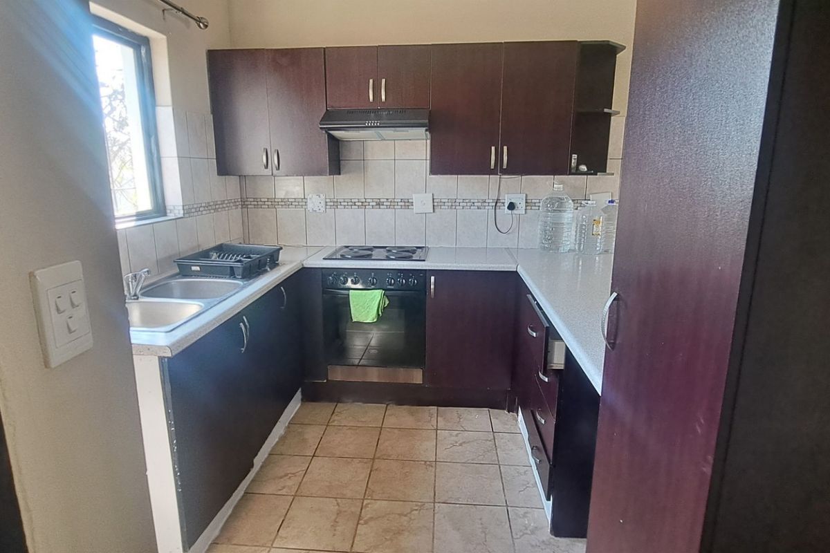 A functional kitchen featuring dark wood cabinetry, laminate countertops, a built-in oven with hob, and tiled flooring.