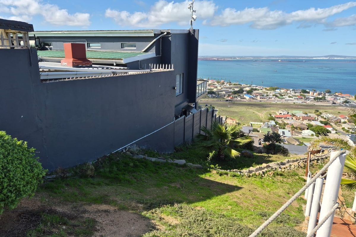 Rear exterior view of the property featuring a dark painted facade, chimney, and security spikes, overlooking a coastal landscape and residential area.