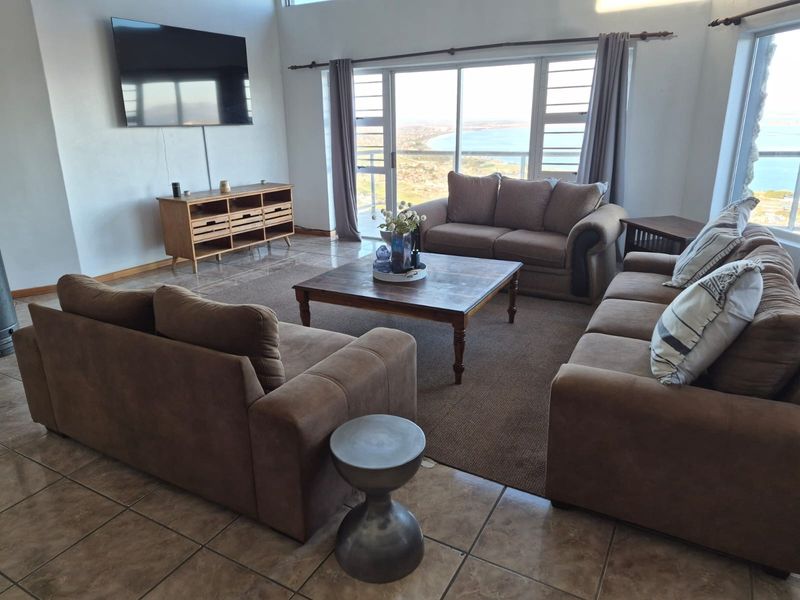 Spacious living room featuring tiled flooring, high ceilings, and large sliding glass doors that offer expansive coastal views.