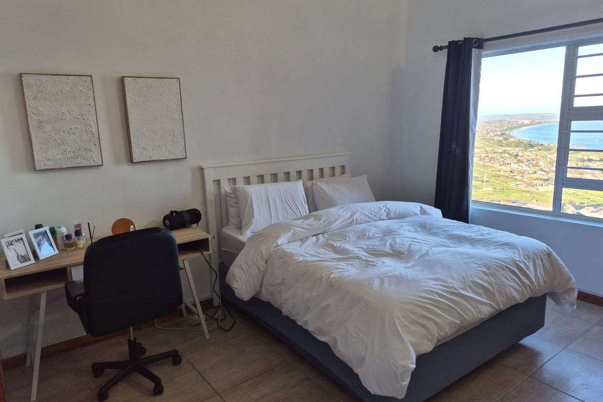 A bright bedroom featuring tiled flooring and a large window offering expansive coastal views.