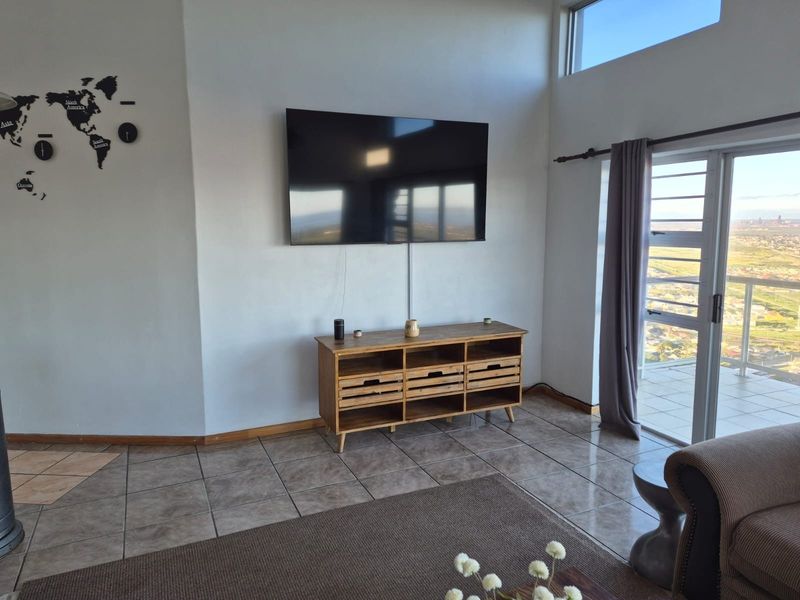 A bright living room featuring tiled flooring, a high-level clerestory window, and a sliding glass door providing access to an outdoor balcony.