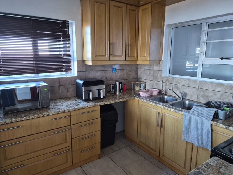 A functional kitchen featuring wood-look laminate cabinetry, granite countertops, a double stainless steel sink, and tiled backsplash with neutral floor tiles.
