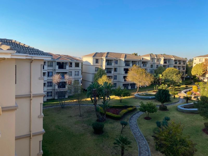 An elevated view of the apartment complex grounds, featuring well-maintained landscaped gardens, paved pathways, and multiple residential building blocks.