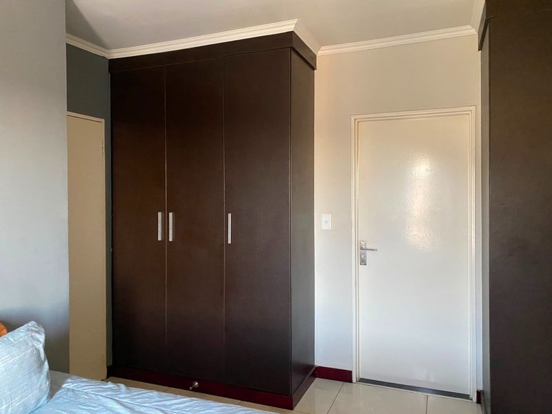 A bedroom featuring dark wood built-in wardrobes, crown molding, and neutral tiled flooring.
