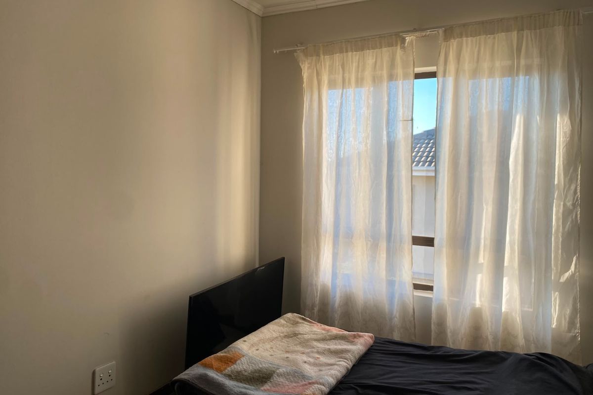 A bedroom featuring a window with curtain rod and wall-mounted electrical outlet, providing natural light and a neutral foundation for interior design.