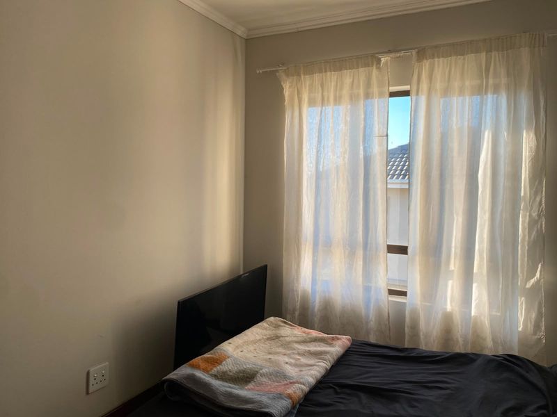 A bedroom featuring a window with curtain rod and wall-mounted electrical outlet, providing natural light and a neutral foundation for interior design.