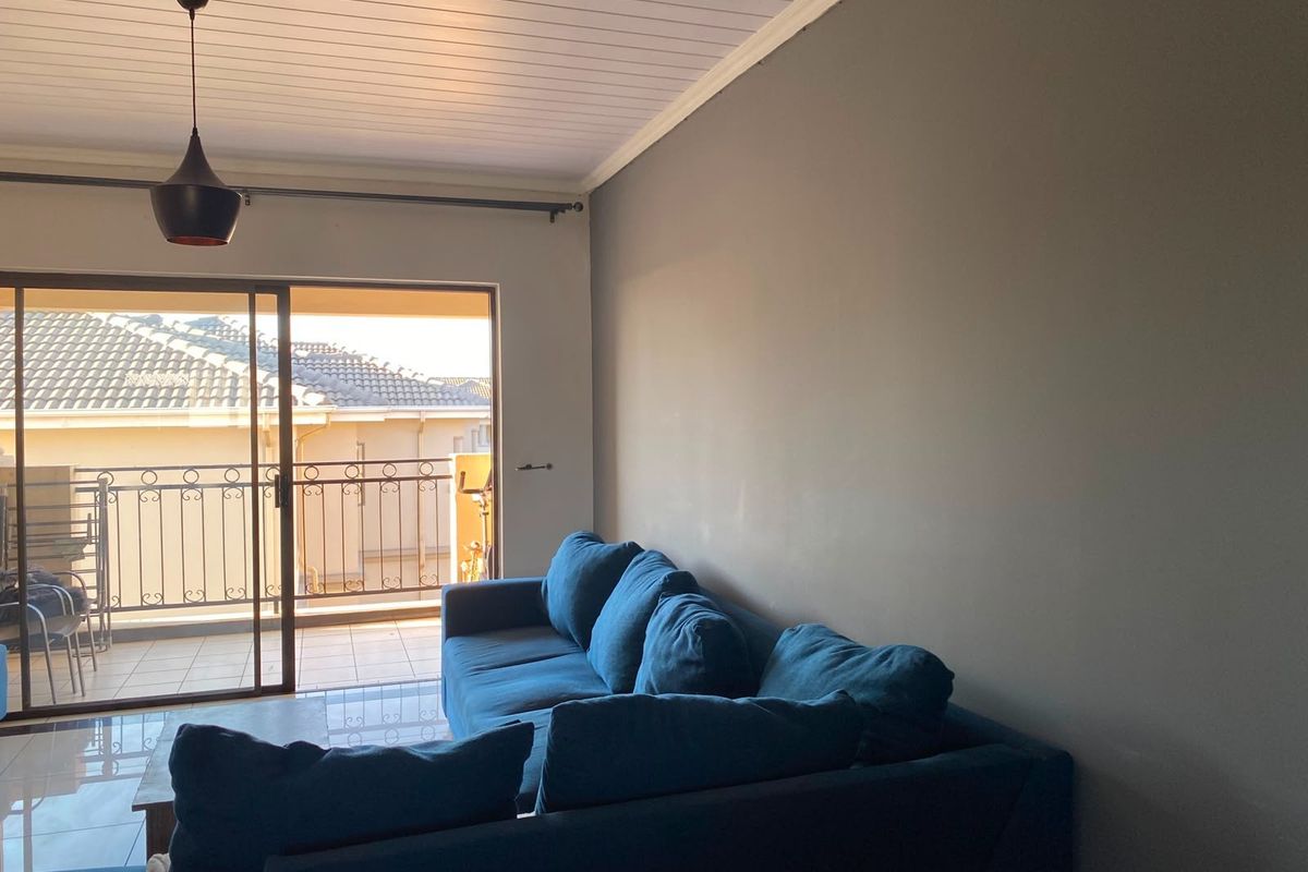 A bright living room featuring tiled floors, a tongue and groove ceiling, and a large sliding glass door leading to a balcony.