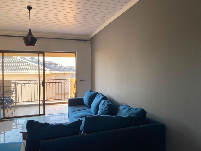A bright living room featuring tiled floors, a tongue and groove ceiling, and a large sliding glass door leading to a balcony.