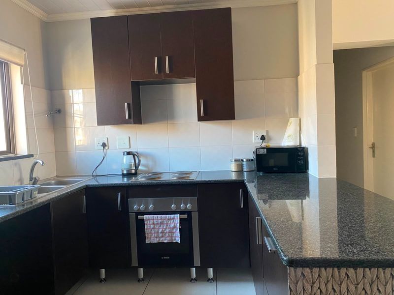 A functional kitchen featuring dark wood cabinetry, granite countertops, a built-in oven with electric hob, and a double sink with tiled backsplash.